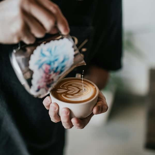 An over-head shot of someone making a latte with frothed milk from a jug